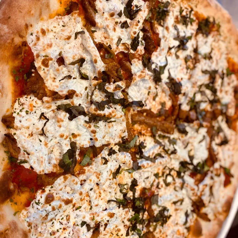 Close-up of a Biaggio Pizzeria pizza with ricotta cheese, tomato sauce, and basil.