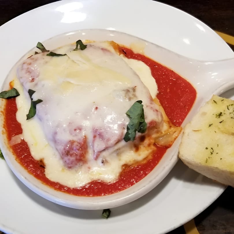 Baked Italian lasagna with melted mozzarella cheese, tomato sauce, fresh basil, and a side of garlic bread.