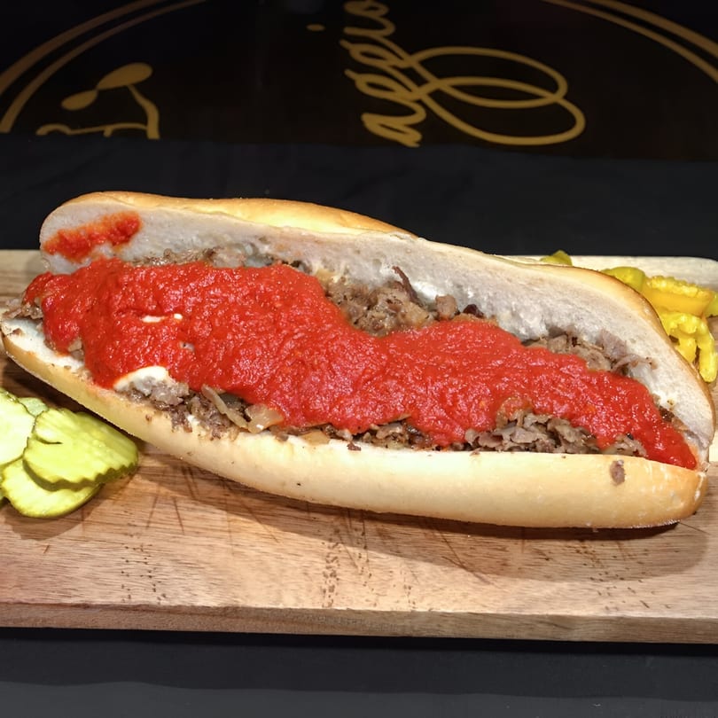 A Biaggio Pizzeria & Family Restaurant cheesesteak with red sauce and pickles on a wooden board.