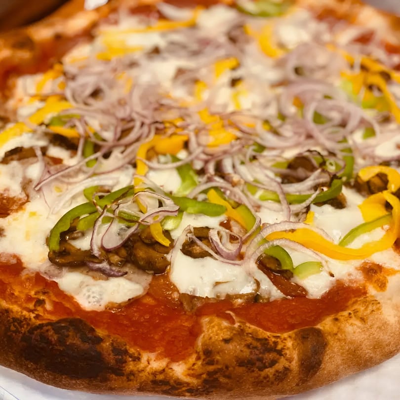 Close-up of a Biaggio Pizzeria pizza with melted cheese, red sauce, onions, and colorful bell peppers.