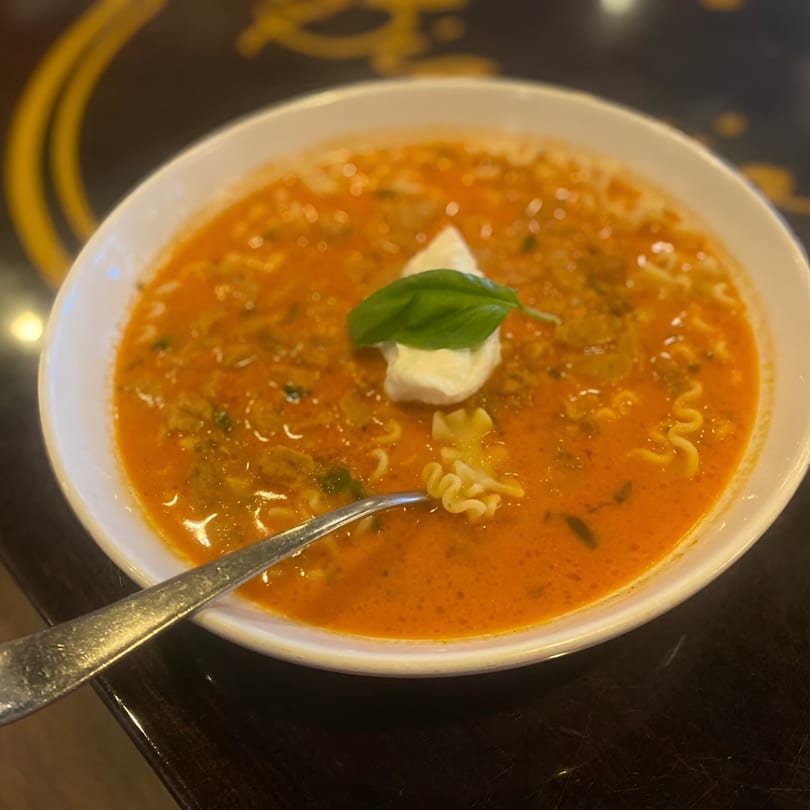 A bowl of Biaggio Pizzeria's tomato soup with pasta, a dollop of cream, and basil.