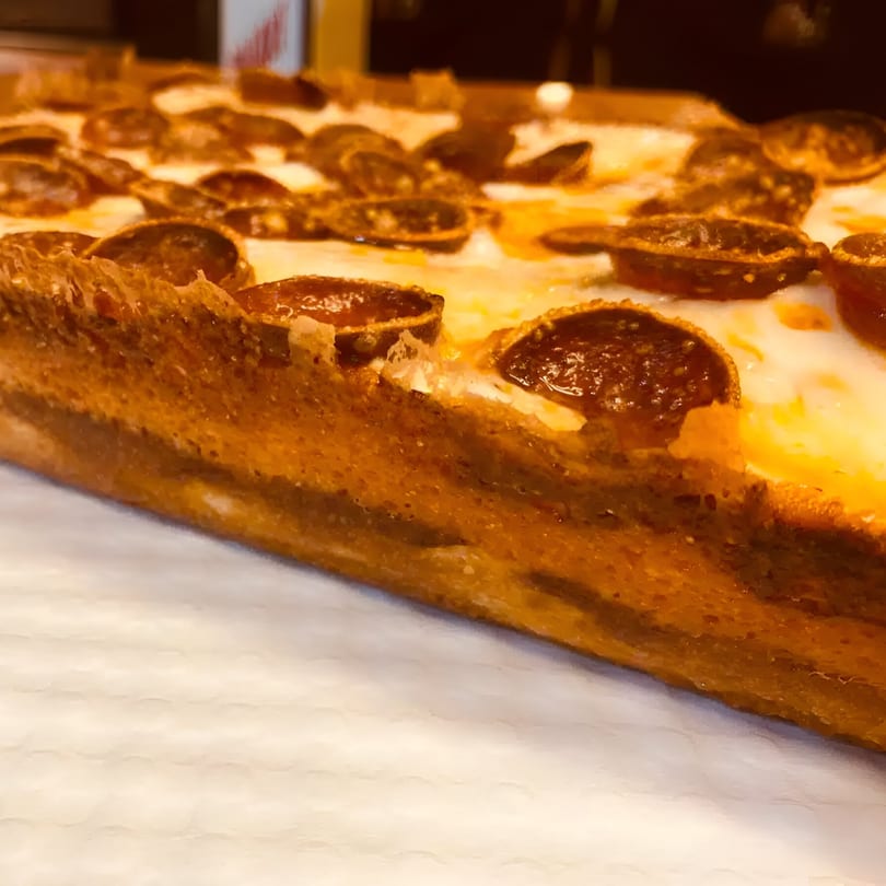 Close-up of a thick-crust pepperoni pizza slice from Biaggio Pizzeria, showcasing crispy edges and melted cheese.
