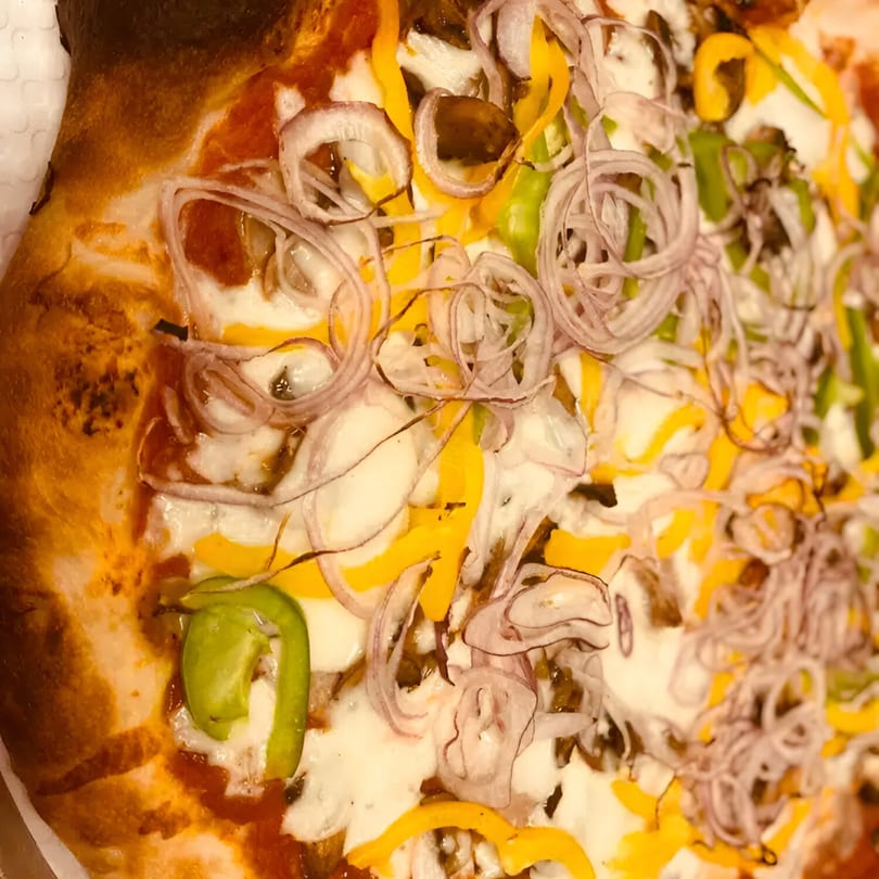 Close-up of a Biaggio Pizzeria pizza with melted cheese, red onions, green, and yellow bell peppers.