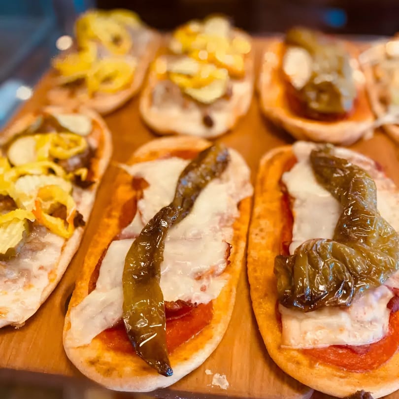 Mini Italian pizzas with melted cheese, tomato sauce, and various pepper toppings on a wooden board.