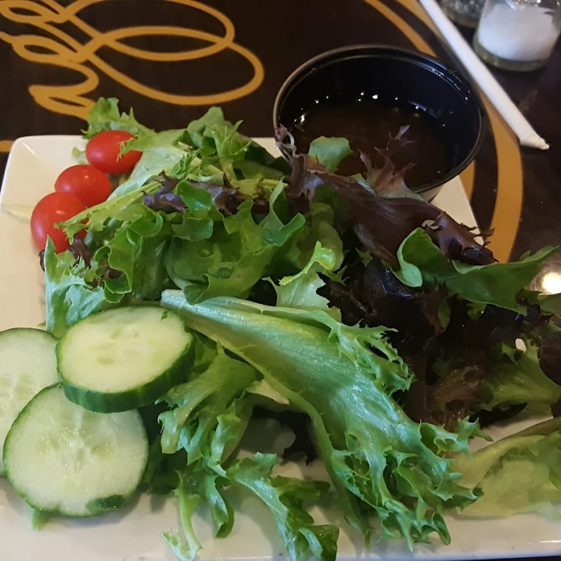 Side salad with mixed greens, cherry tomatoes, and cucumber slices, with dressing on the side.