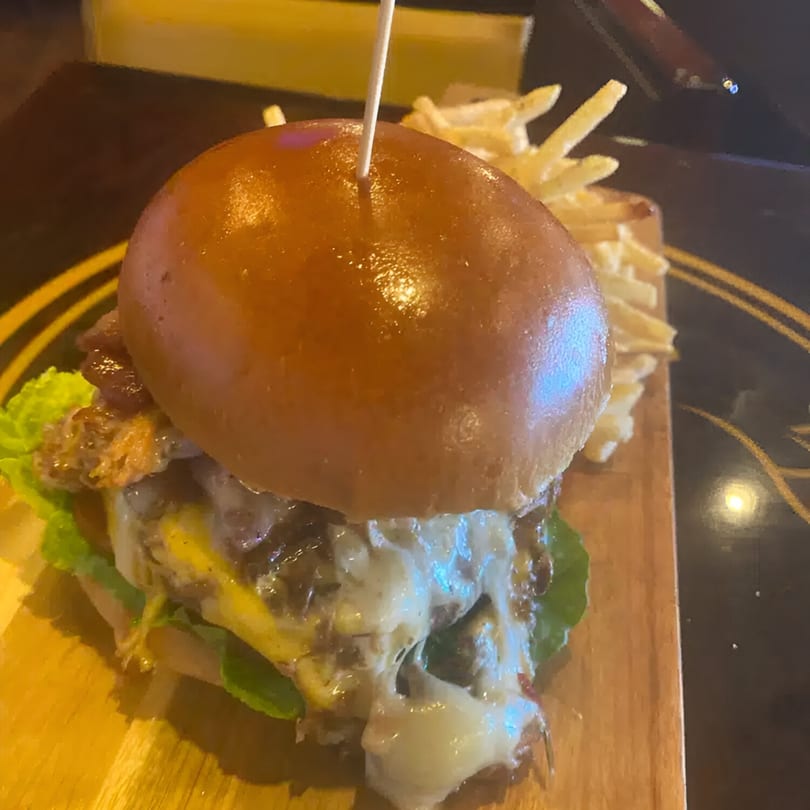 A juicy burger with melted cheese, lettuce, and bacon, served with a side of fries on a wooden board.