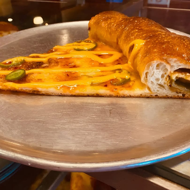 A slice of Biaggio Pizzeria's cheesy pizza with jalapeños and a rolled crust on a metal tray.