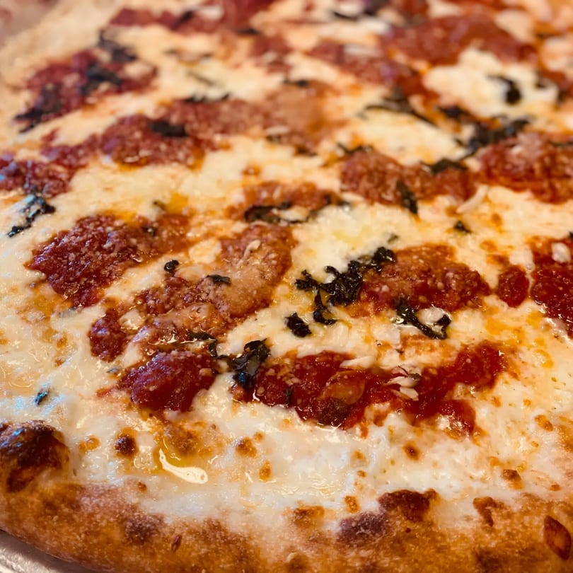 Close-up of a Biaggio Pizzeria pizza with melted cheese, red sauce, and basil.