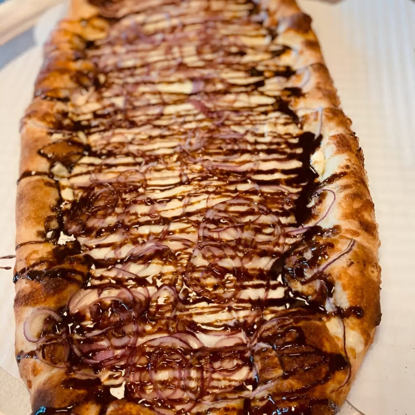 Rectangular Biaggio Pizzeria flatbread with white sauce, red onions, and a balsamic glaze drizzle.
