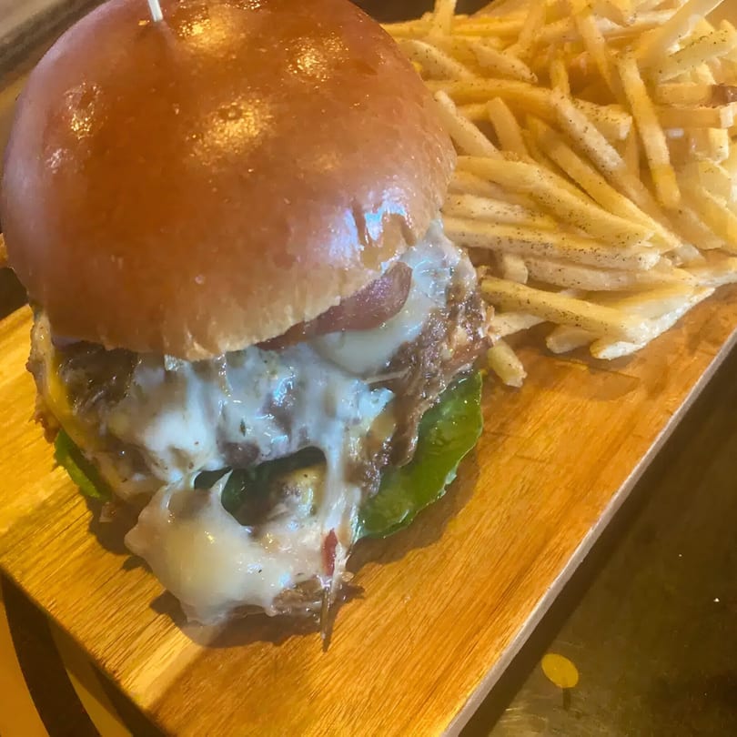A juicy burger with melted cheese and bacon, served with a side of crispy fries on a wooden board.